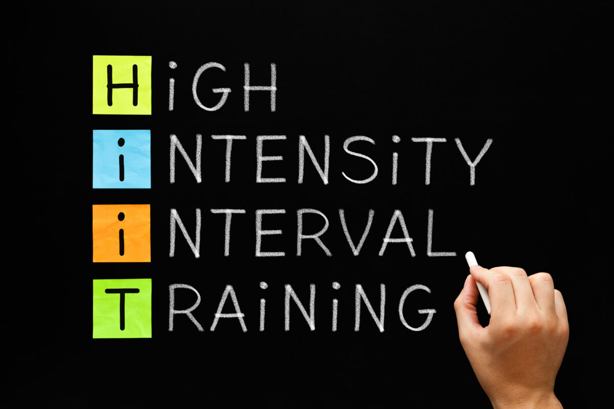 Hand writing fitness workout acronym HIIT - High Intensity Interval Training with white chalk on blackboard.