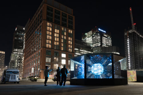 The artwork Geist lights up a blue sphere against a dark city landscape